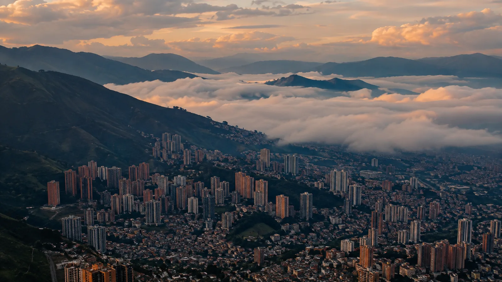 An Andean valley city at sunrise seen from the surrounding ridges, with low cloud filling the valley floor.